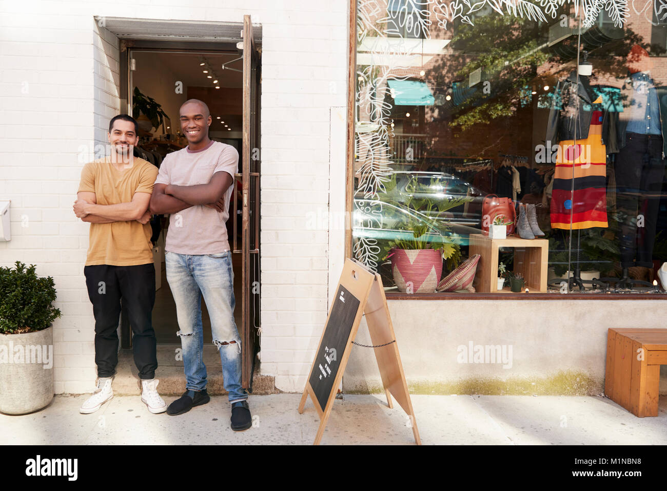 Deux jeunes hommes smiling to camera à l'extérieur de leur magasin de vêtements Banque D'Images