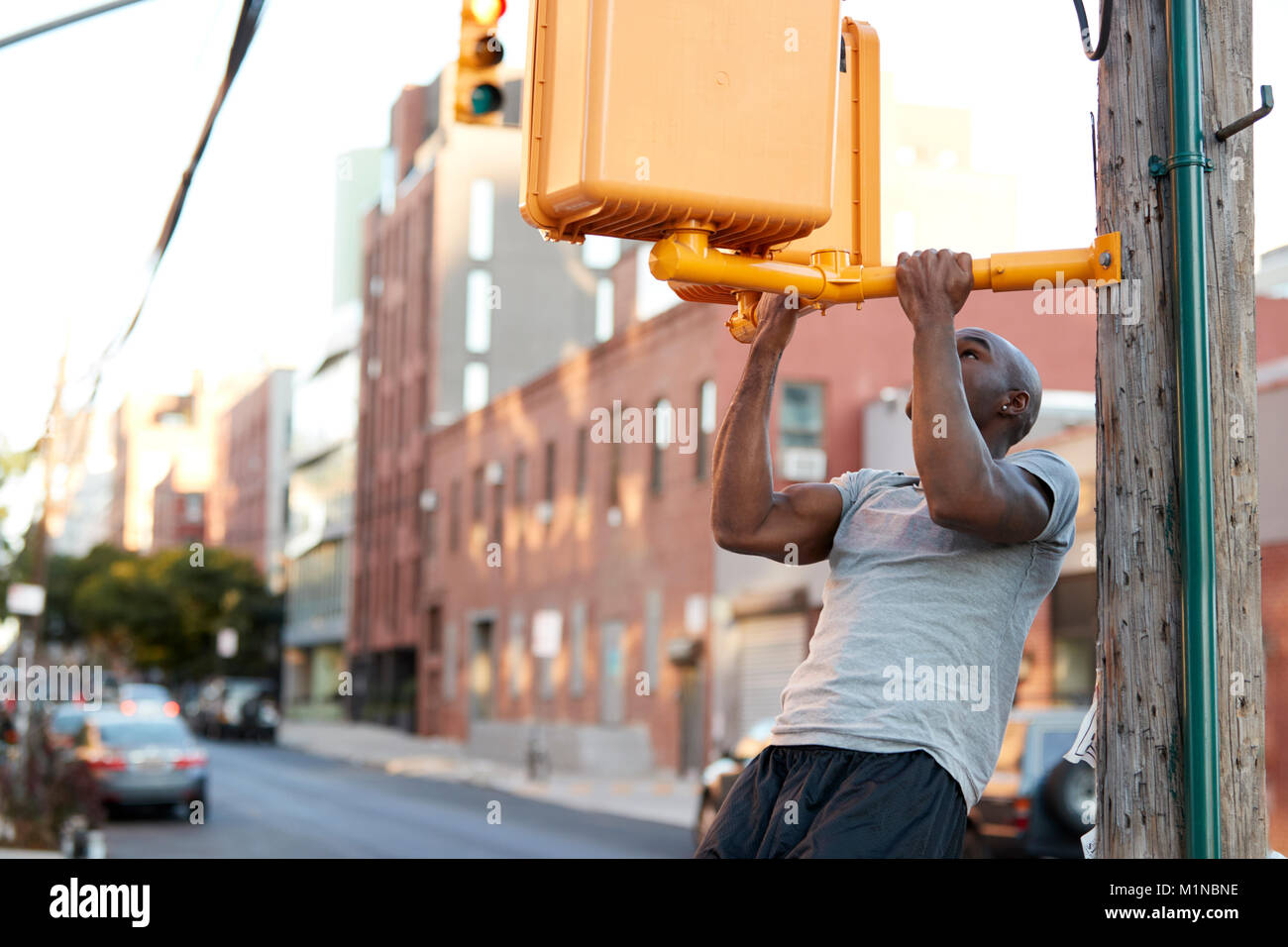 Jeune homme noir faisant chin ups de traverser la rue dans la lumière Banque D'Images