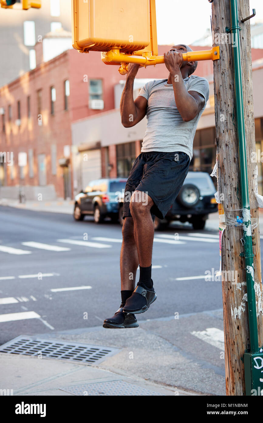 Jeune homme noir faisant chin ups à Brooklyn street, vertical Banque D'Images