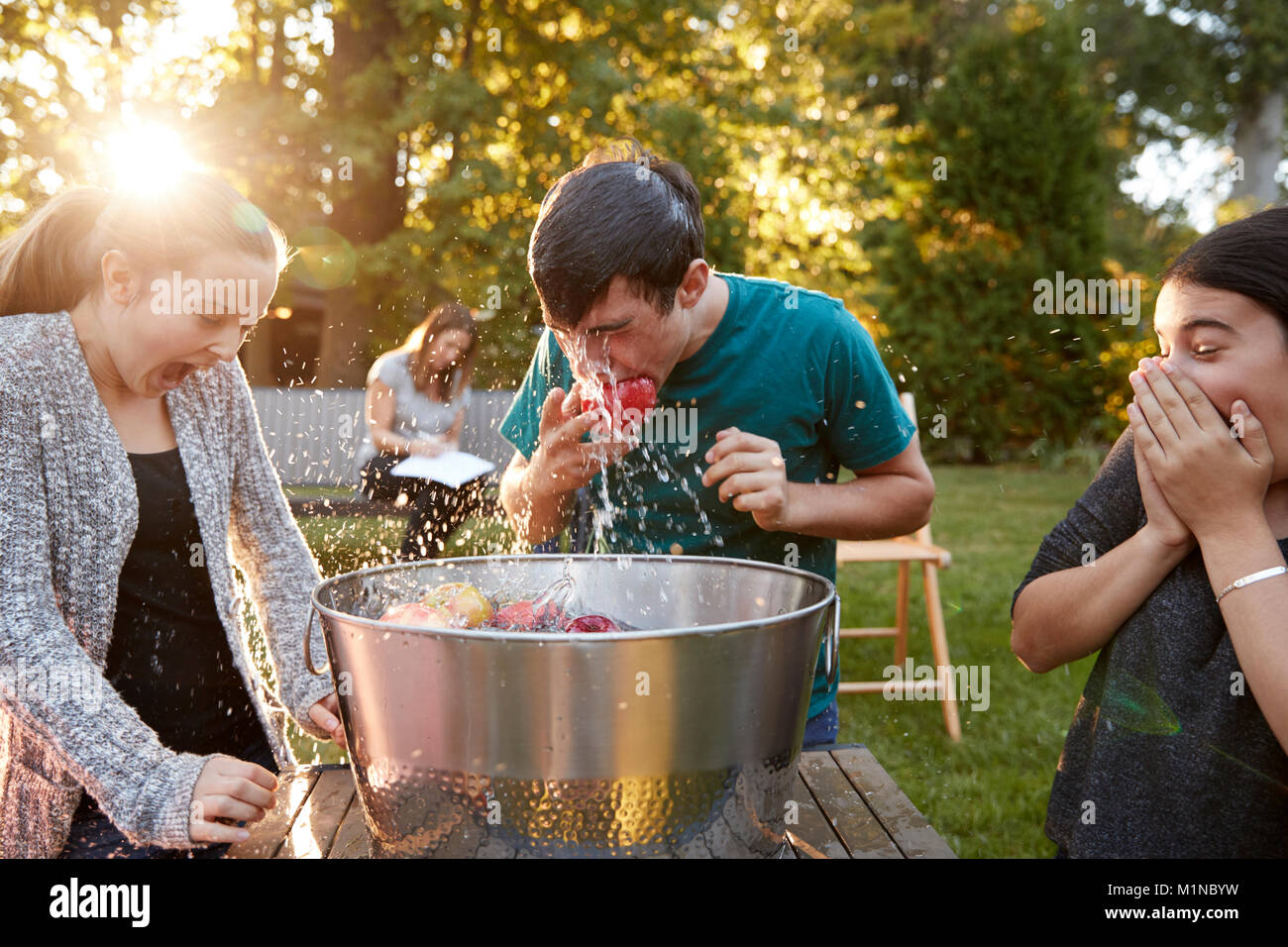 Les amis regarder adolescent pendillant apple at garden party Banque D'Images