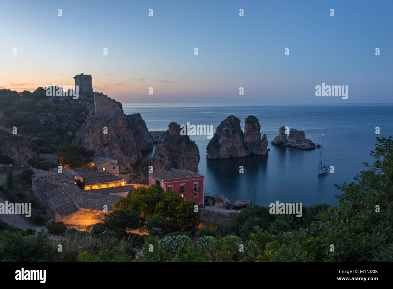 La Tonnara immeuble avec petite plage surplombé par les ruines et les faraglioni dans la mer Méditerranée au crépuscule à Scopello, Sicile, Italie. Banque D'Images
