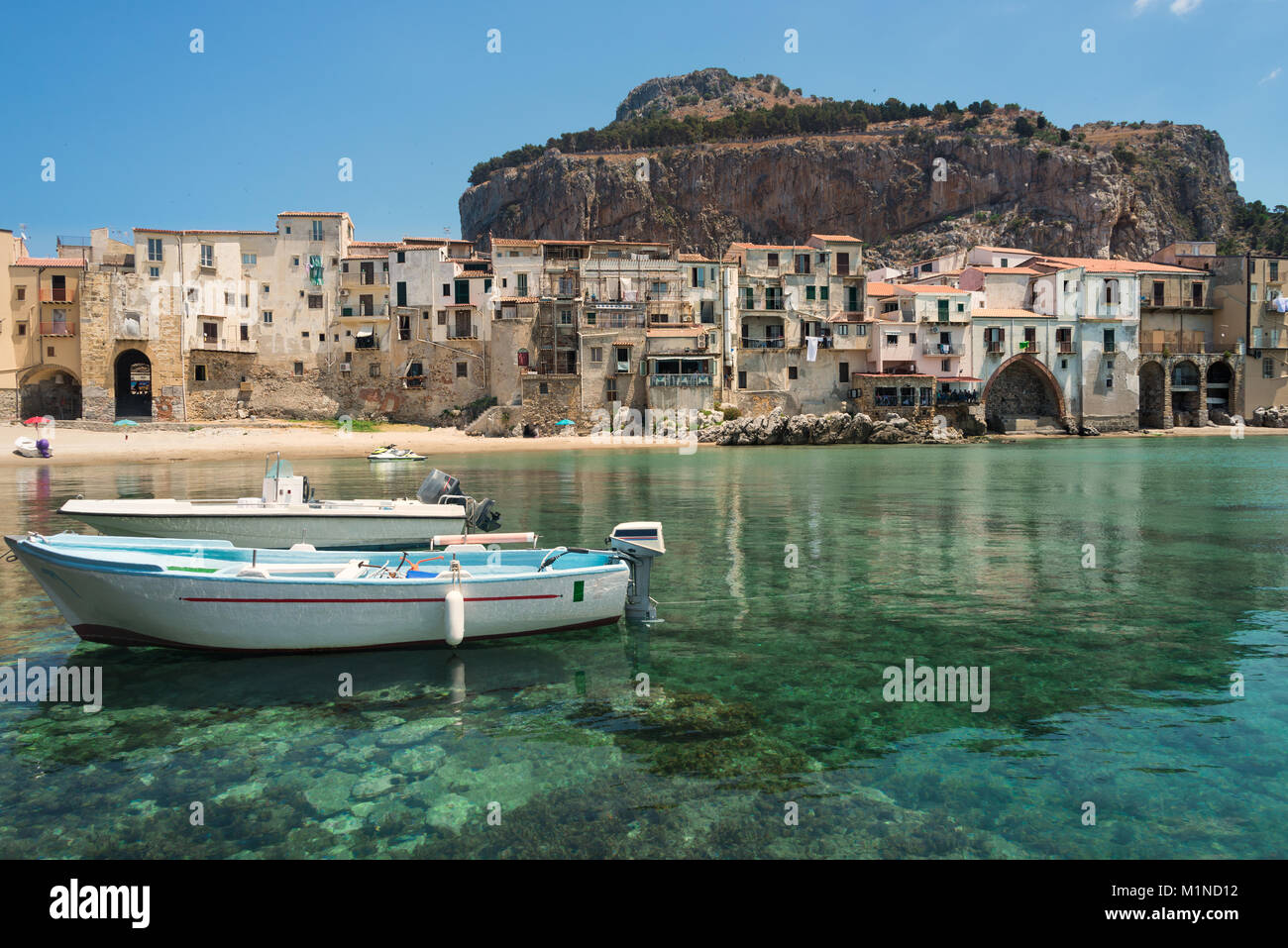 Deux bateaux canot dans les eaux vert émeraude du petit port à la plage de la ville, dans la vieille ville de Cefalu près de Palerme en Sicile, Italie. Banque D'Images