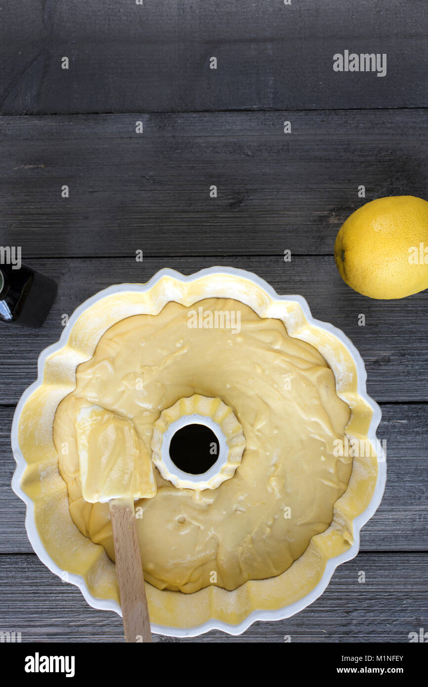 Préparation de la pâte pour un gâteau au citron dans un moule bundt jaune avec une spatule sur une table rustique Banque D'Images