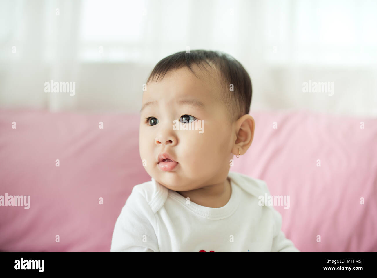 Sweet baby girl sitting on bed at home. Banque D'Images