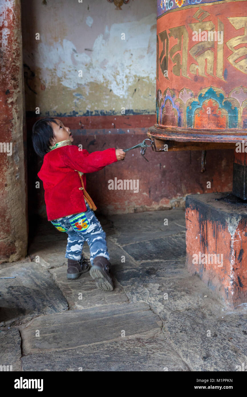 Bumthang, Bhoutan. Petit garçon tirant de grandes prières, Jambay Monastère Lhakhang. Banque D'Images