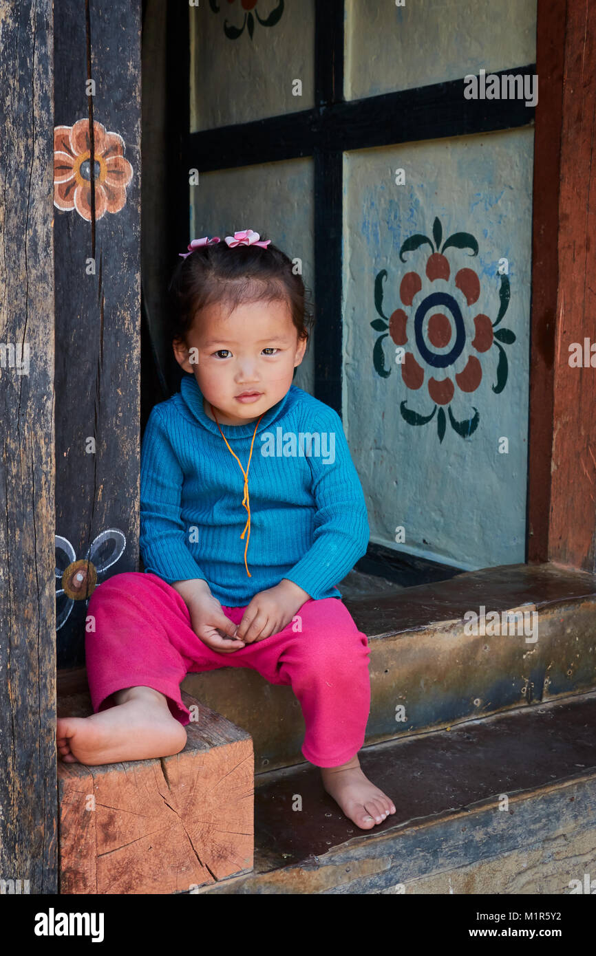 Petite fille assise à la porte de chambre de porter haut bleu et rose en butée au Bhoutan Banque D'Images