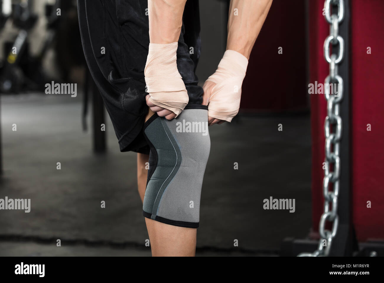 Close-up d'une personne de la préparation pour la formation de porter un bandage au genou dans la salle de sport Banque D'Images