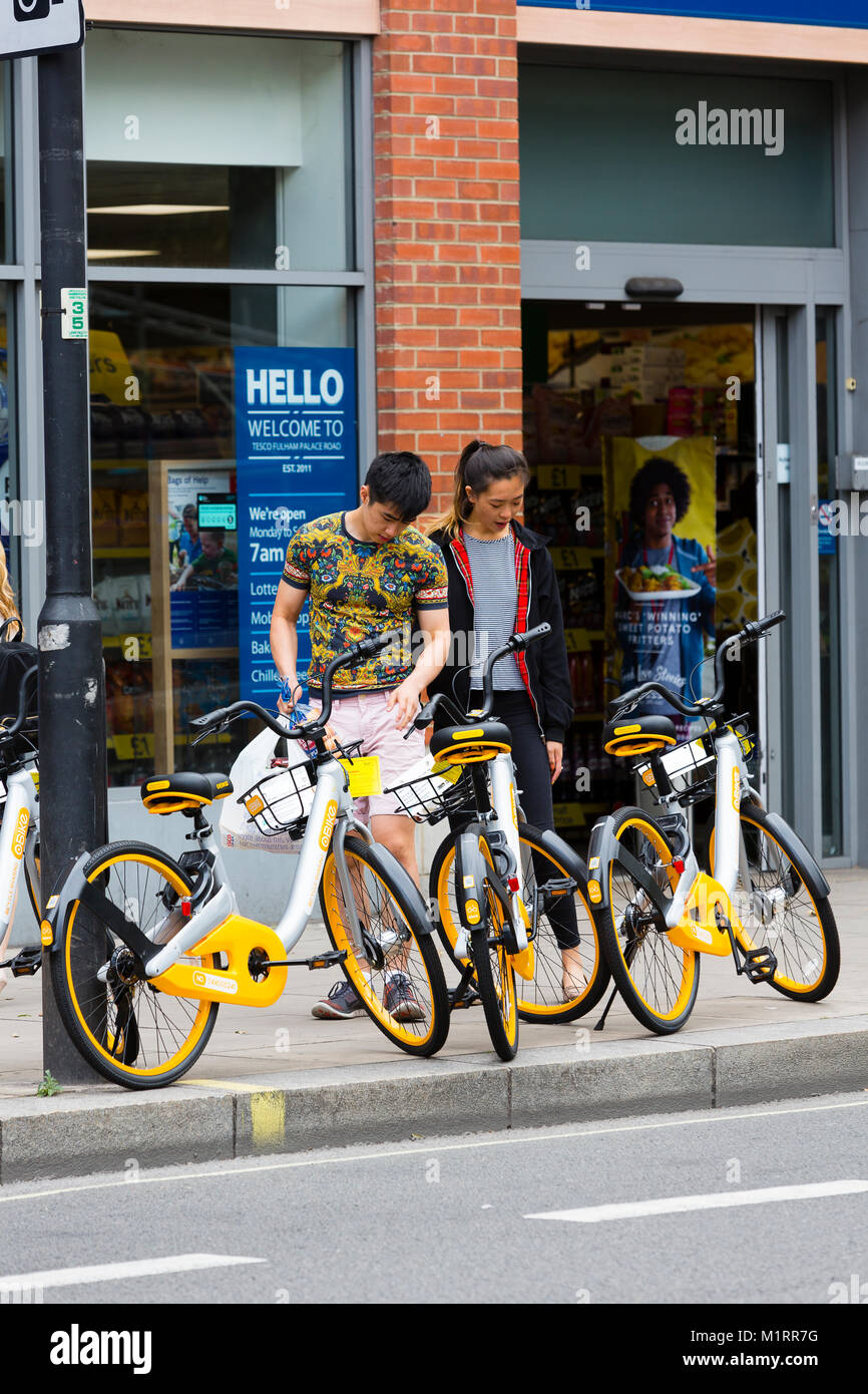 Londres, Angleterre. Un couple à Fulham pause pour lire un avis indiquant que l'obstruction du Obike les bicyclettes sont un obstacle. Banque D'Images