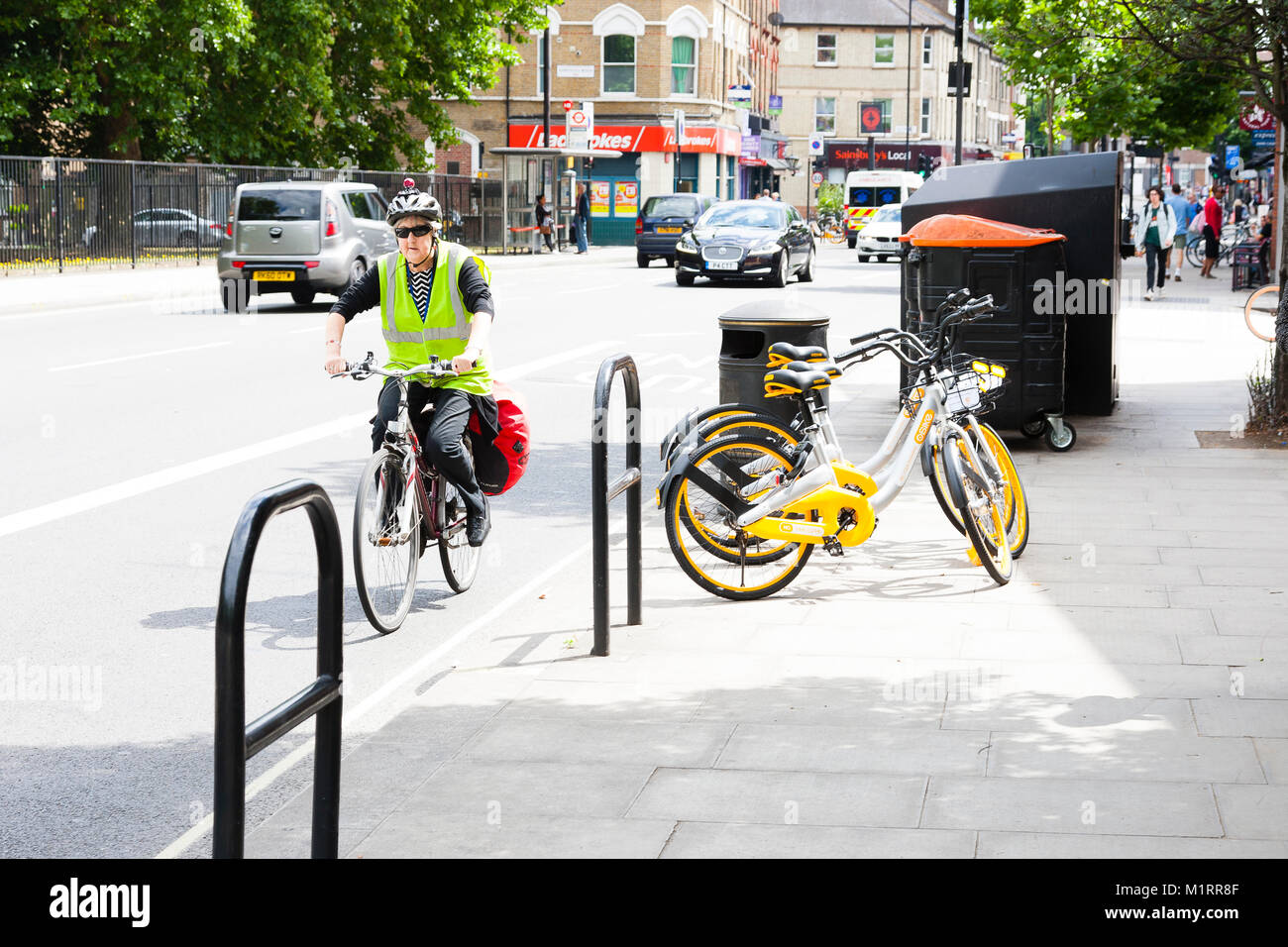 Londres, Angleterre. Un cycliste rides passé un trio de Obikes non utilisés à Fulham après le service de lancement. Banque D'Images