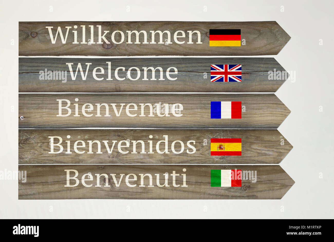 Pancarte en bois montrant bienvenue dans cinq langues différentes avec leurs drapeaux et indications sur fond gris clair Banque D'Images