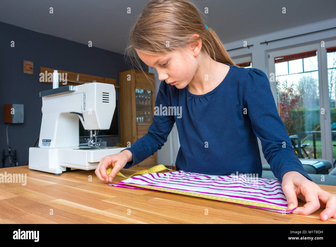 Portrait d'une fillette de 8 ans mesurant un tissu rayé rose et blanc avec un ruban à mesurer Banque D'Images