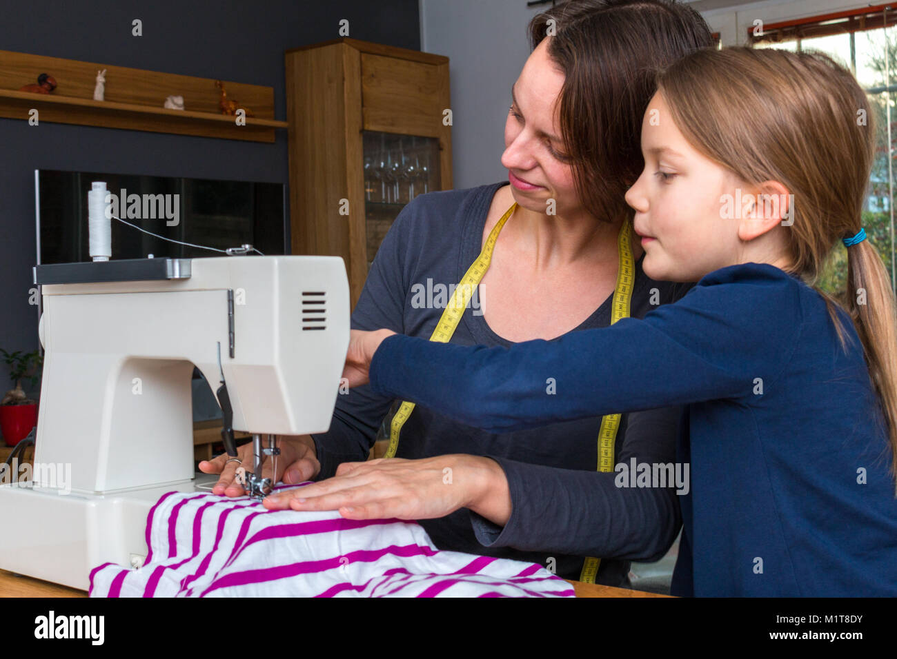Mère, fille de 8 ans comment coudre une fabics à rayures avec une machine à coudre Banque D'Images