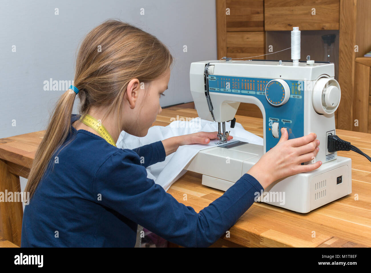 Une fillette de 8 ans est une couture textile blanc. Main droite appuie sur le bouton de rembobinage Banque D'Images