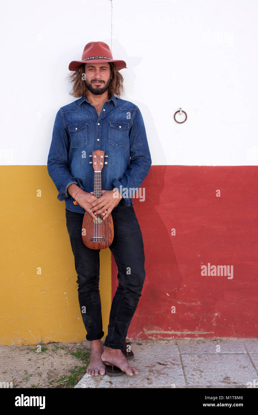 Dans Red Hat Cowboy appuyé contre un wll colorés tenant un ukulele Banque D'Images