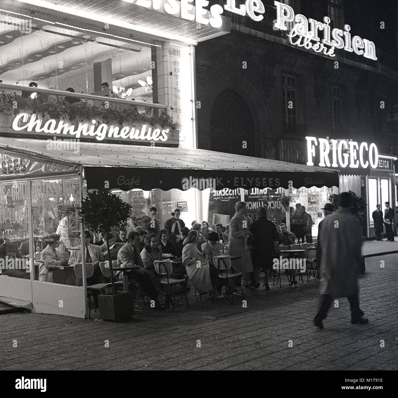 Années 1950, la société historique, café....soir-temps à Paris et les parisiens prendre un verre et de conversation dans une terrasse de café sur le trottoir d'une rue pavée, près de l'Avenue des Champs-Elysées. Banque D'Images