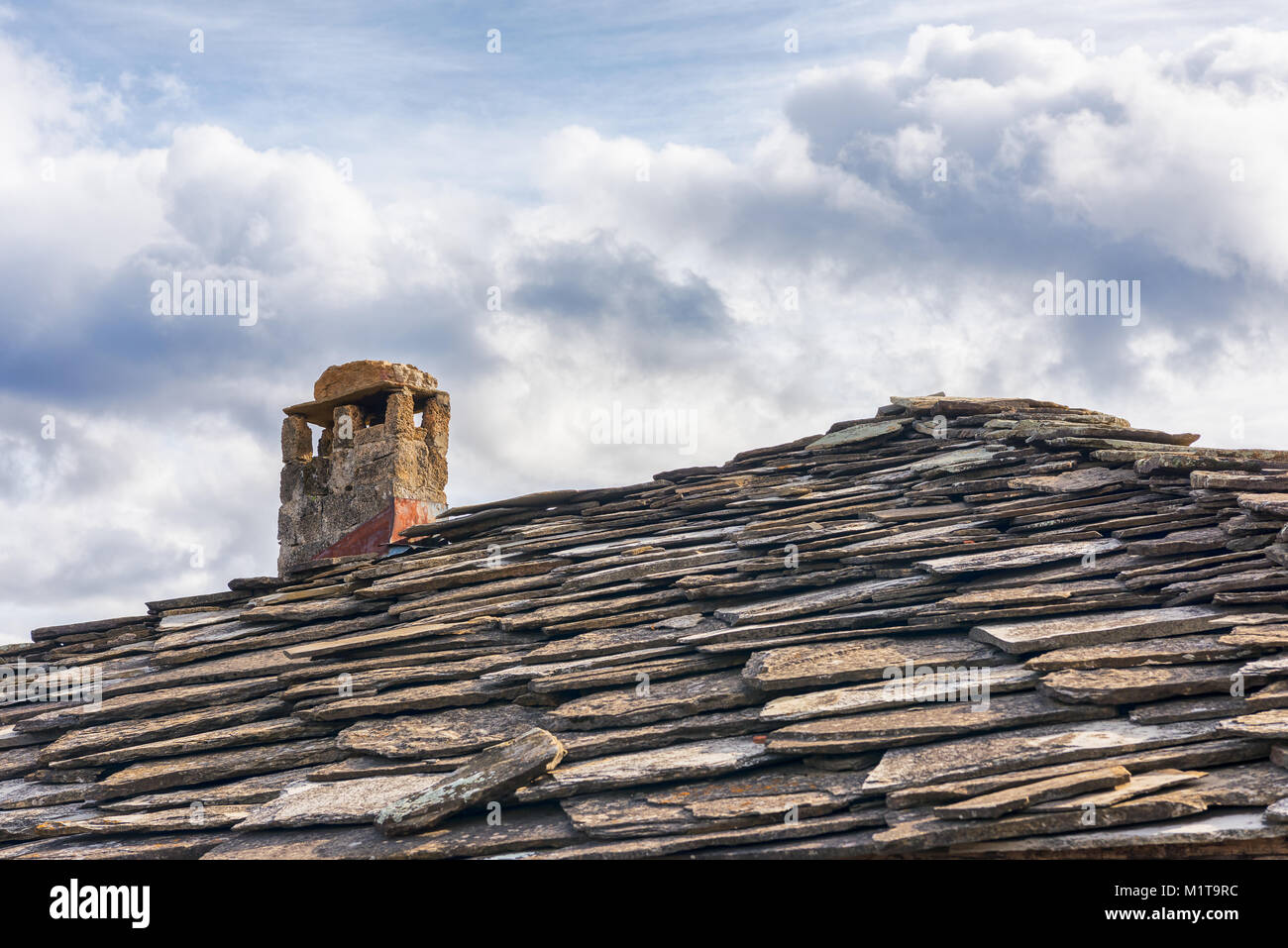 Toit en ardoise ; toiture en tuiles en pierre et cheminée contre ciel nuageux Banque D'Images
