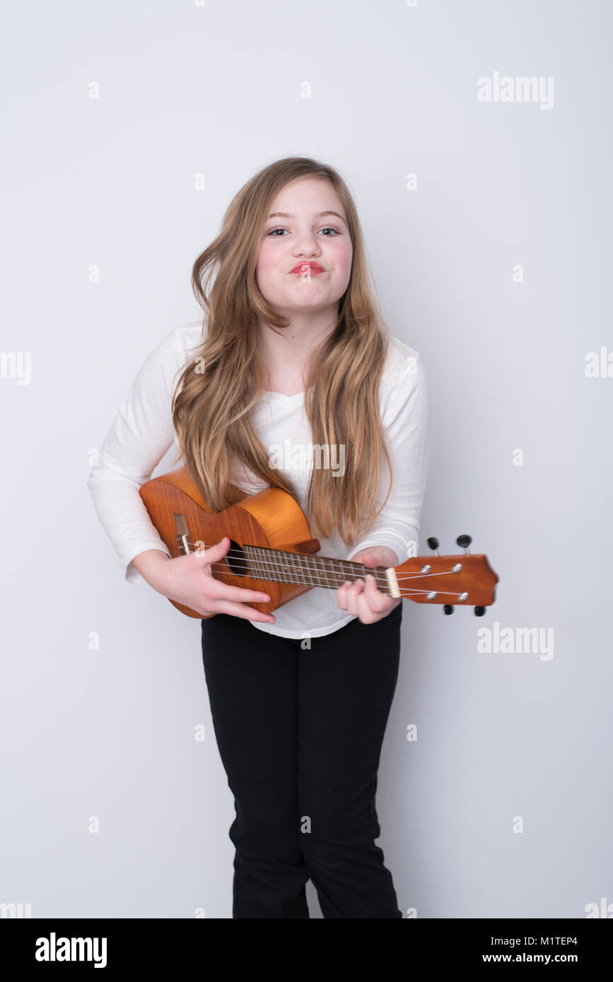 Fille avec vos lèvres pincées dans l'expression ludique jouer ukulele sur fond blanc Banque D'Images