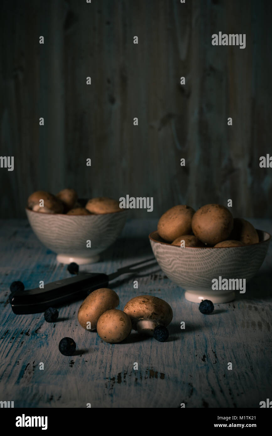 Photo verticale avec plusieurs faire revenir les champignons. Certains d'entre eux sont dans des bols en céramique. D'autres champignons sont déversés sur vintage wooden board avec quelques blackth Banque D'Images