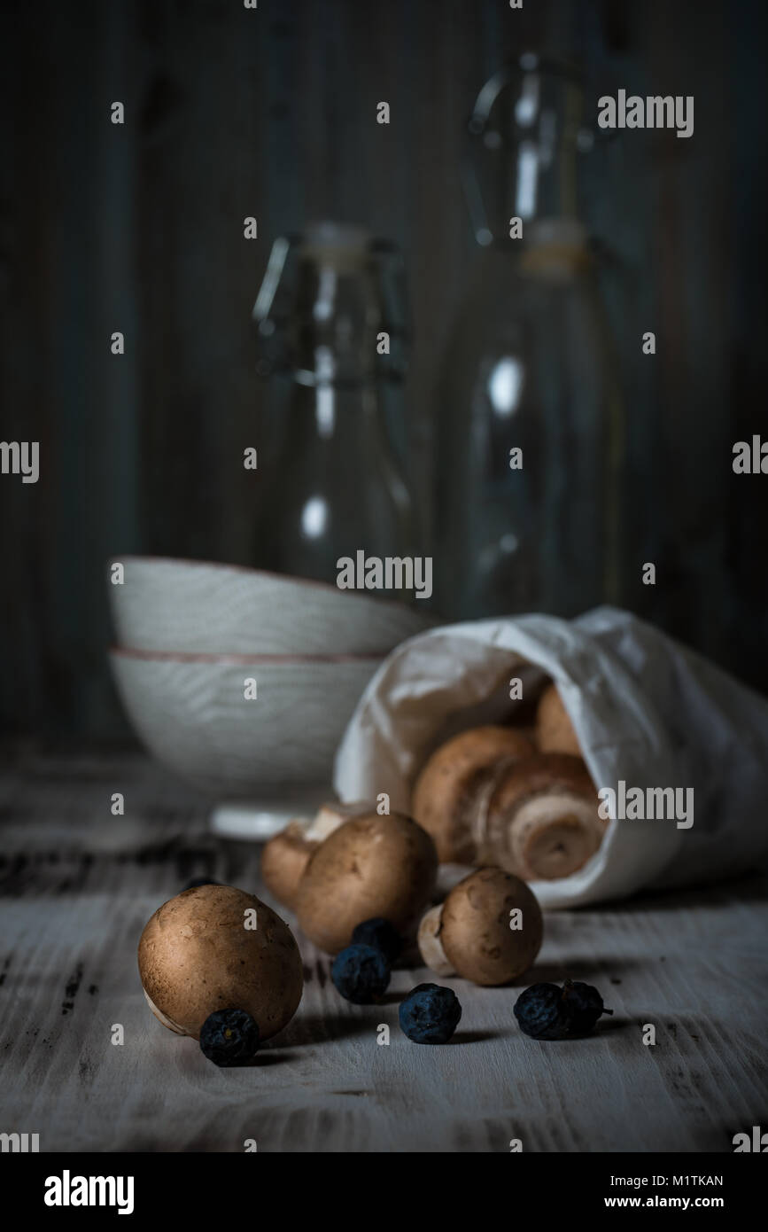 Photo verticale avec brun déversé des champignons comestibles à partir de sac de papier. Les champignons sont sur vintage planche en bois avec deux bols et deux bo de verre Banque D'Images