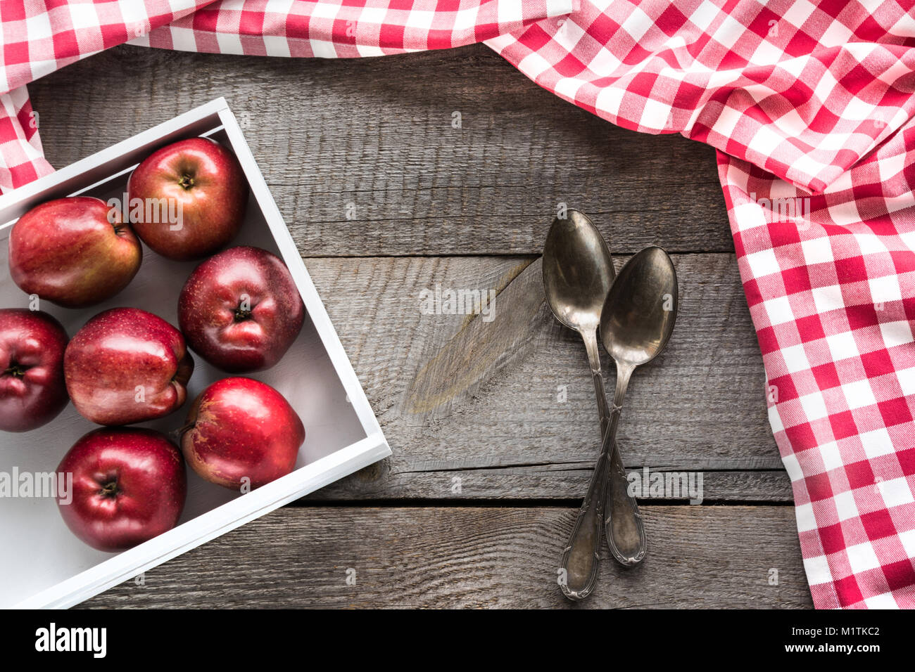 Pommes rouges bien mûrs en bouleau-box sur planche de bois avec une serviette autour de rouge à carreaux, et les cuillères et copie de l'espace pour votre recette. Banque D'Images