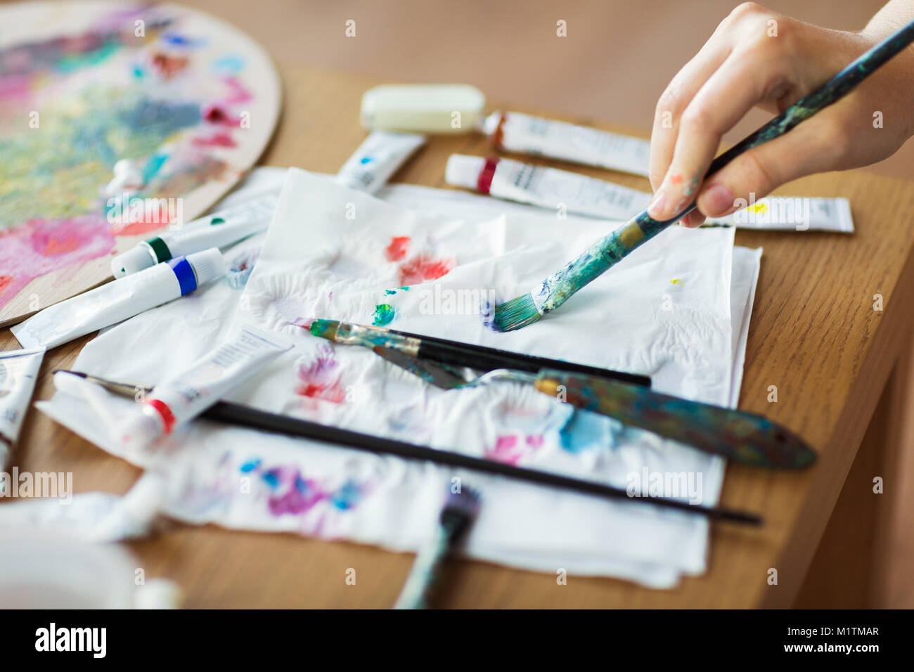 La main de l'artiste avec le pinceau, le papier et les tubes de peinture Banque D'Images
