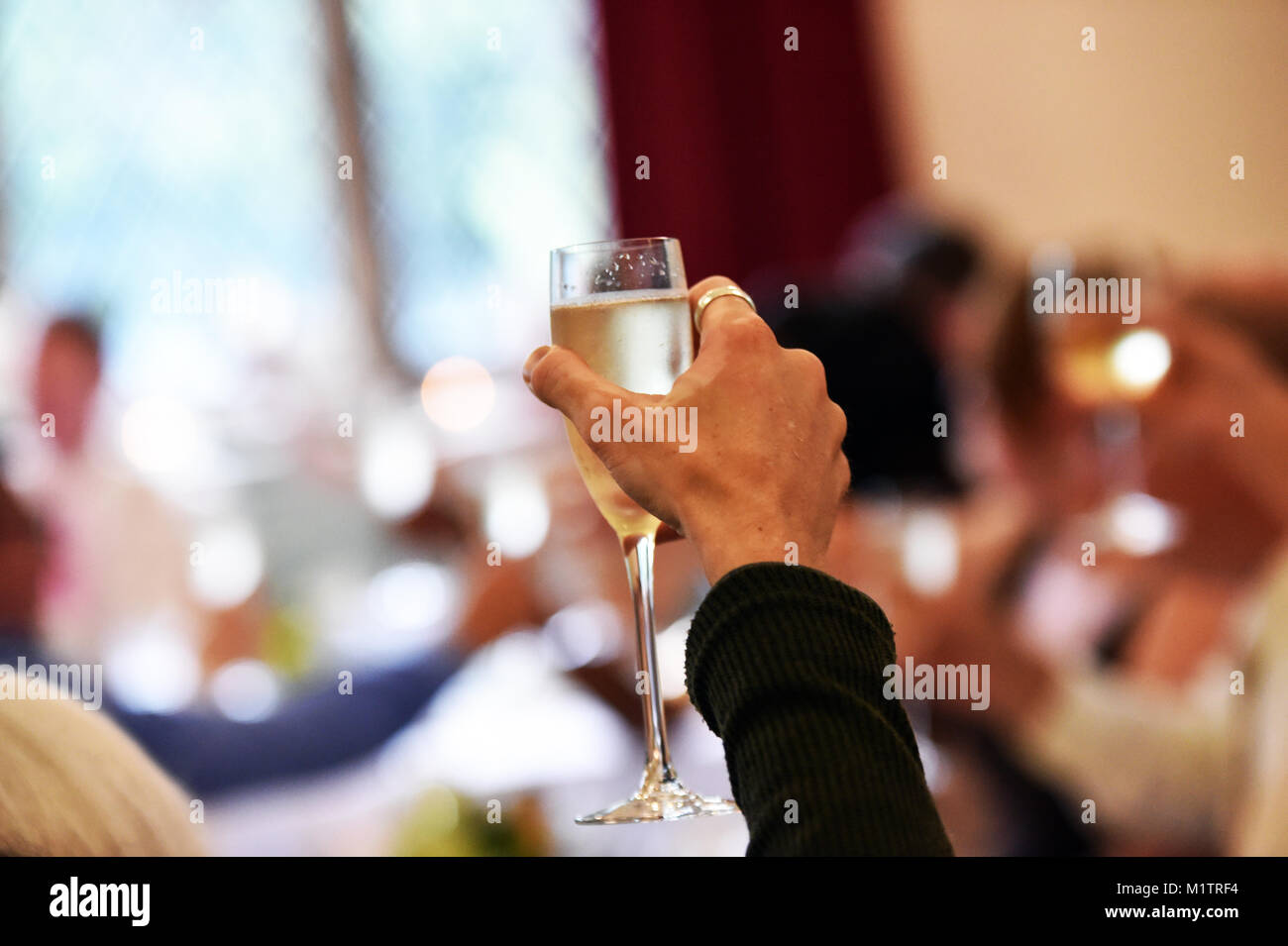 Gros plan d'une main tenant un verre de vin à la mariée et le marié à une réception de mariage Banque D'Images