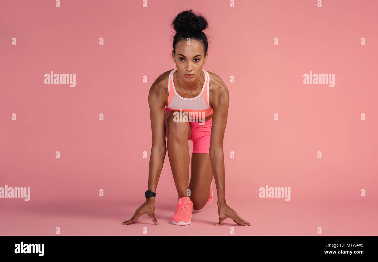 Fit young woman standing en position démarrage sur fond rose. Grande sportive sur le point de commencer une analyse. Banque D'Images