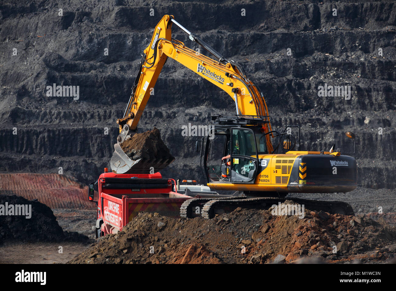 Un excavateur à charger les camions sur l'usine de recyclage du charbon dans Recycoal,Rossington Doncaster qui a été démolie pour faire place à de nouvelles maisons. Banque D'Images