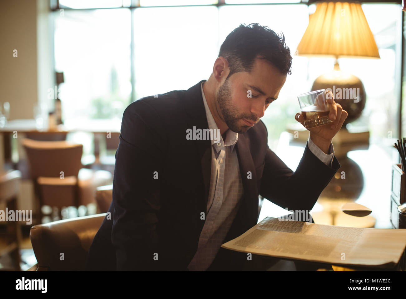 Businessman reading newspaper en tenant un verre de whisky Banque D'Images