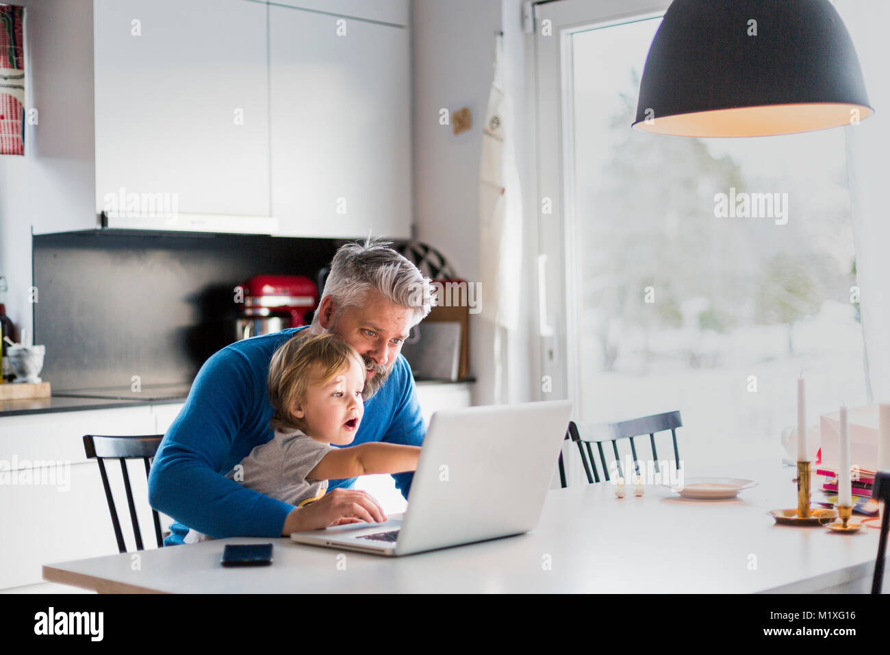 L'homme et l'enfant jouant avec un ordinateur portable dans la cuisine Banque D'Images