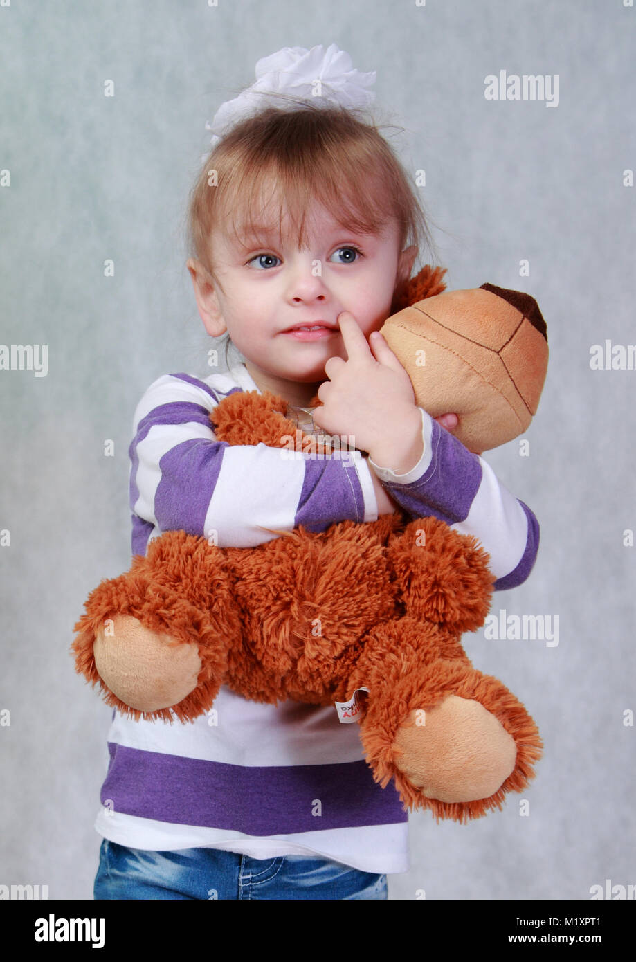 Sur un fond gris est une petite fille et serrant un ours en peluche. Banque D'Images