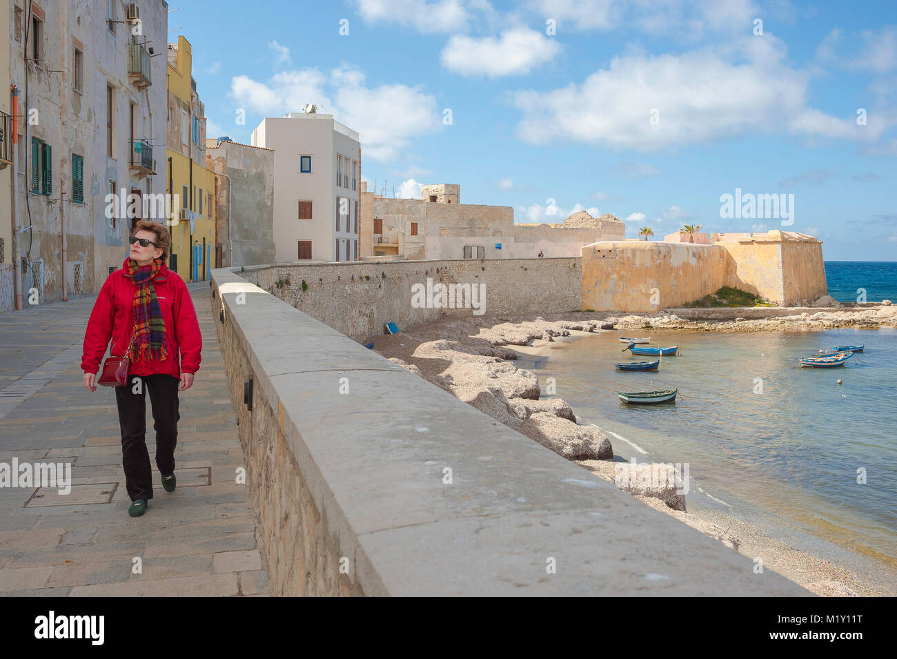 Trapani Sicile mur de mer, vue d'une femme mûre simple marchant le long du mur de mer dans le port de Trapani, Sicile (MODÈLE LIBÉRÉ) Banque D'Images