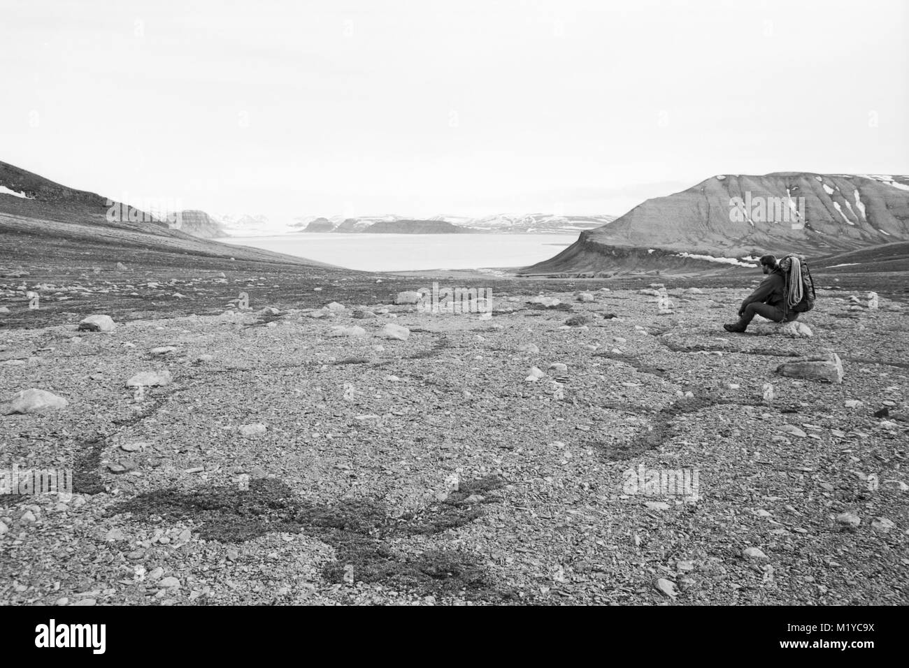 Dans un paysage arctique stérile un homme, vêtu de vêtements de randonnée et de l'exécution cordes d'escalade, est assis sur un petit rocher Banque D'Images