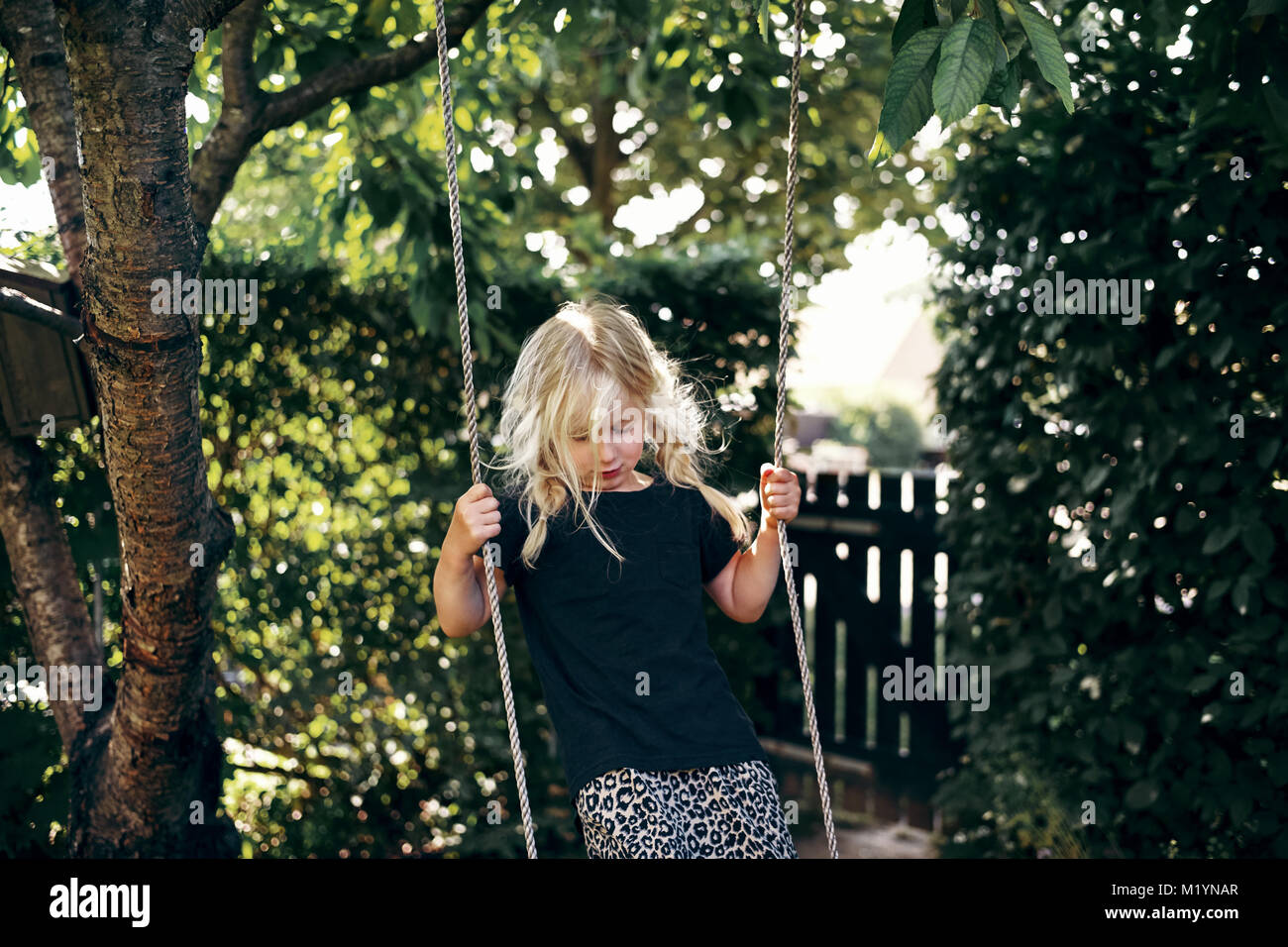 Adorable petite fille blonde accroché sur un arbre en rotation jouer seul  dans sa cour arrière sur une journée ensoleillée Photo Stock - Alamy