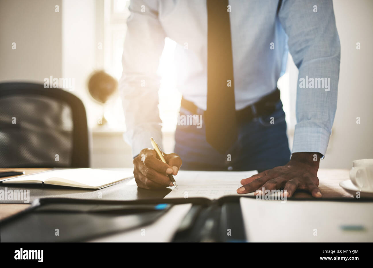 Jeune avocat africain portant une chemise et cravate la signature de  documents tout en s'appuyant sur son bureau dans un bureau Photo Stock -  Alamy