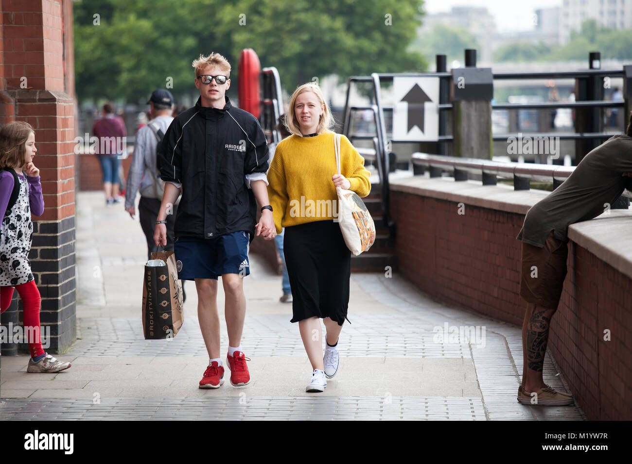 Londres, ANGLETERRE - 22 août 2017 une fille dans un chandail orange et une jupe noire promenades avec son garçon le long de South Bank Banque D'Images