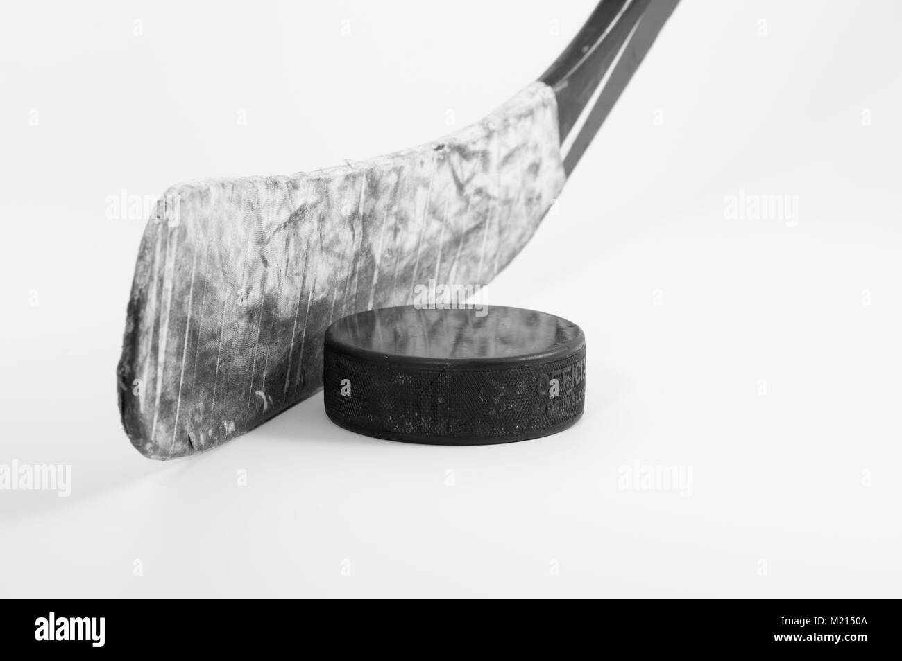 Lame de bâton de hockey sur glace enveloppée d'un ruban blanc et une usure rondelle utilisée sur un fond blanc ; image monochrome Banque D'Images