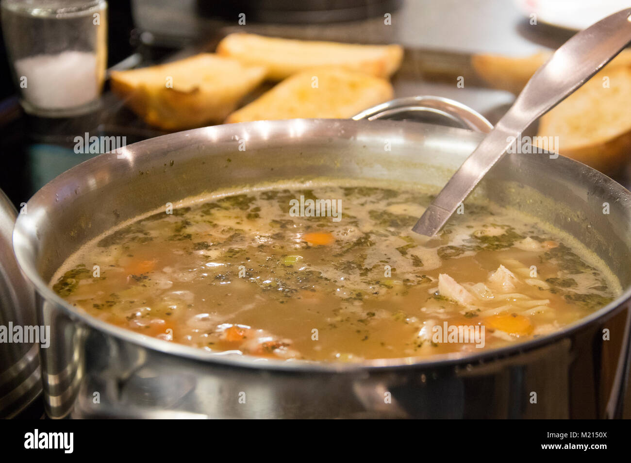 Soupe poulet et nouilles faites maison avec des légumes dans une grande casserole en acier inoxydable avec des tranches de pain grillé à l'arrière-plan Banque D'Images