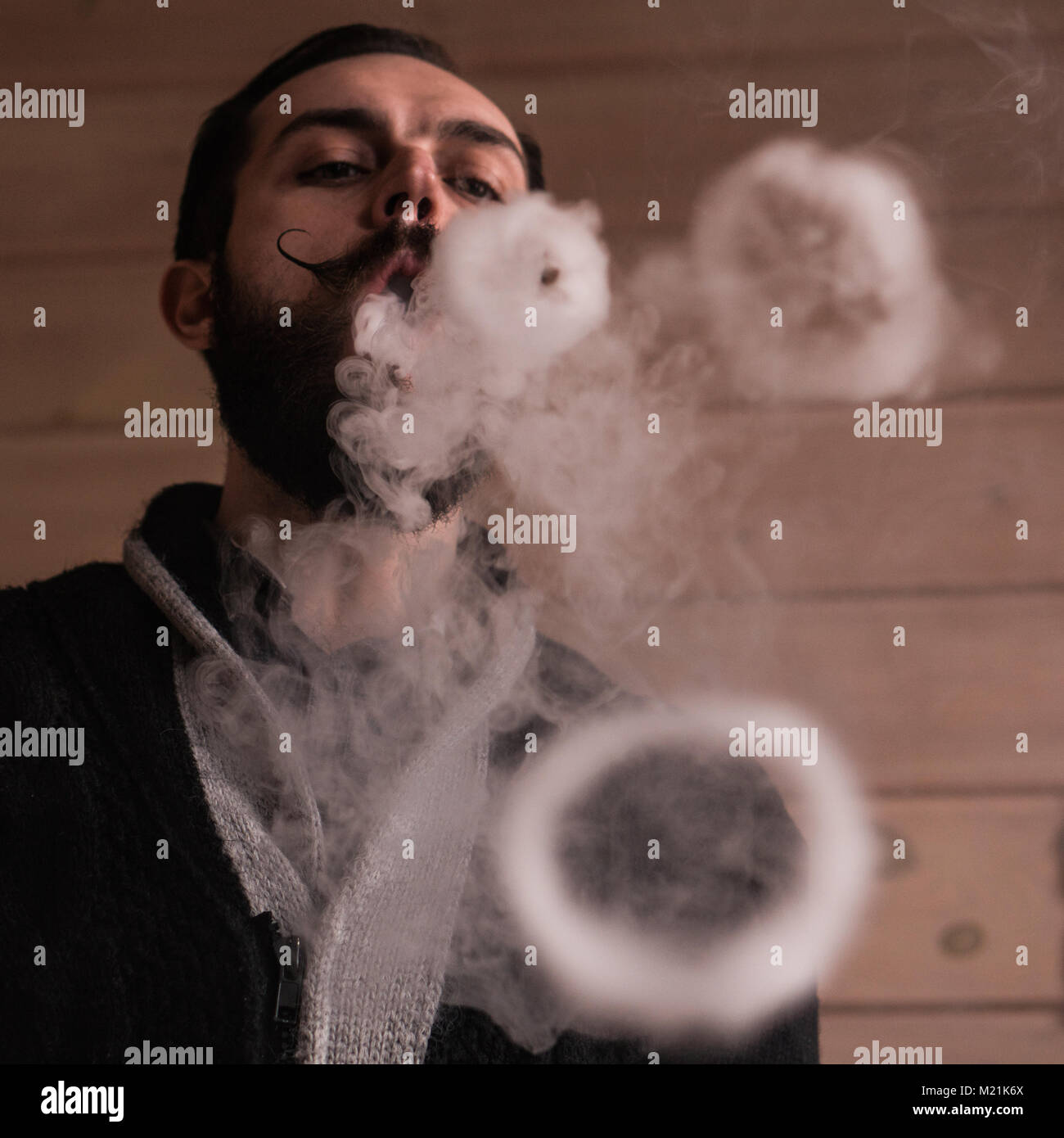 Homme avec Barbe et Mustages Vaping une cigarette électronique. Vaper fumée Hipster vaporisateur et Exhals des ronds de fumée. Banque D'Images