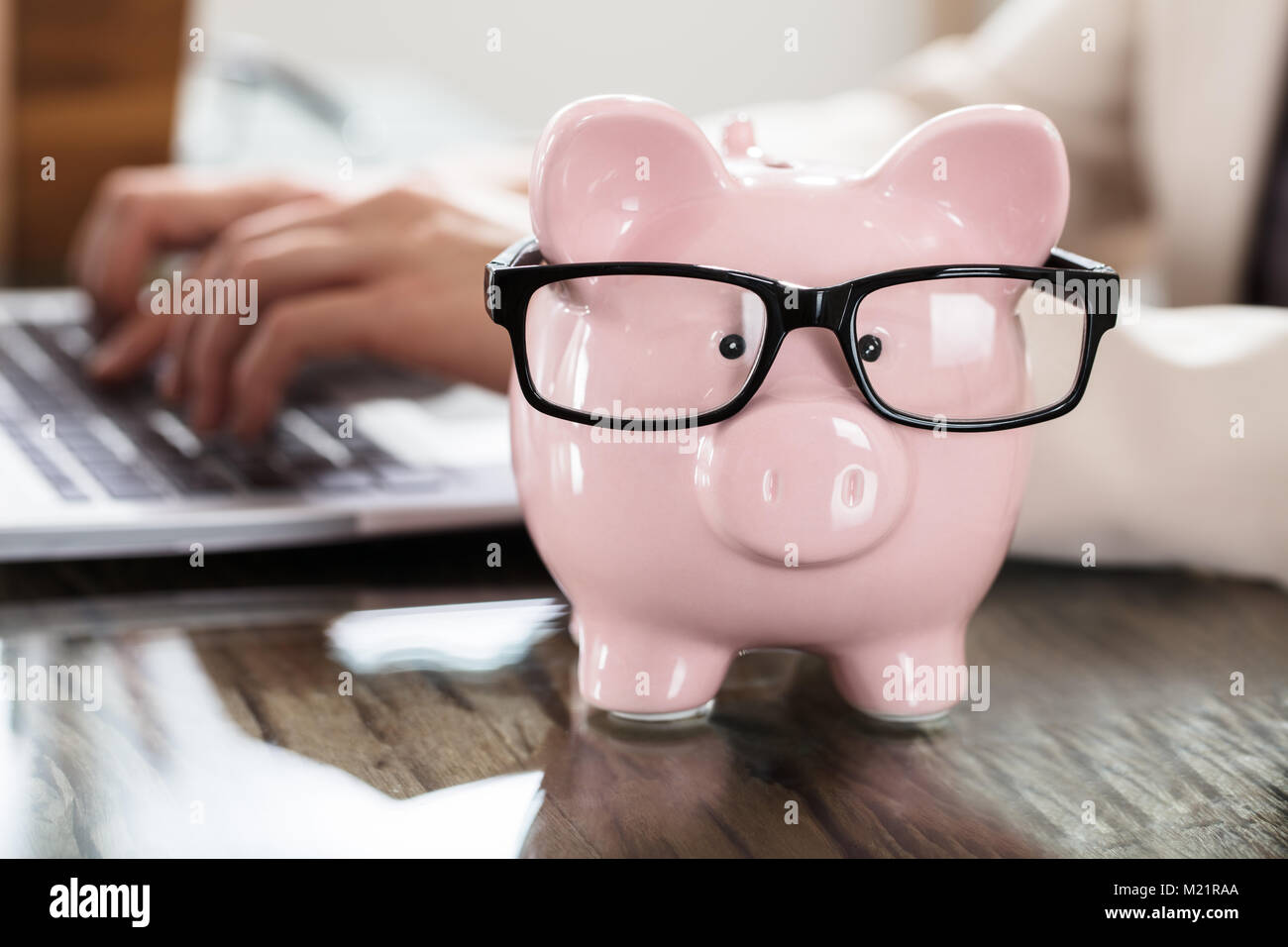 Pink Piggy Bank avec lunettes en face d'une personne d'affaires à l'aide d'ordinateur portable sur le lieu de travail Banque D'Images