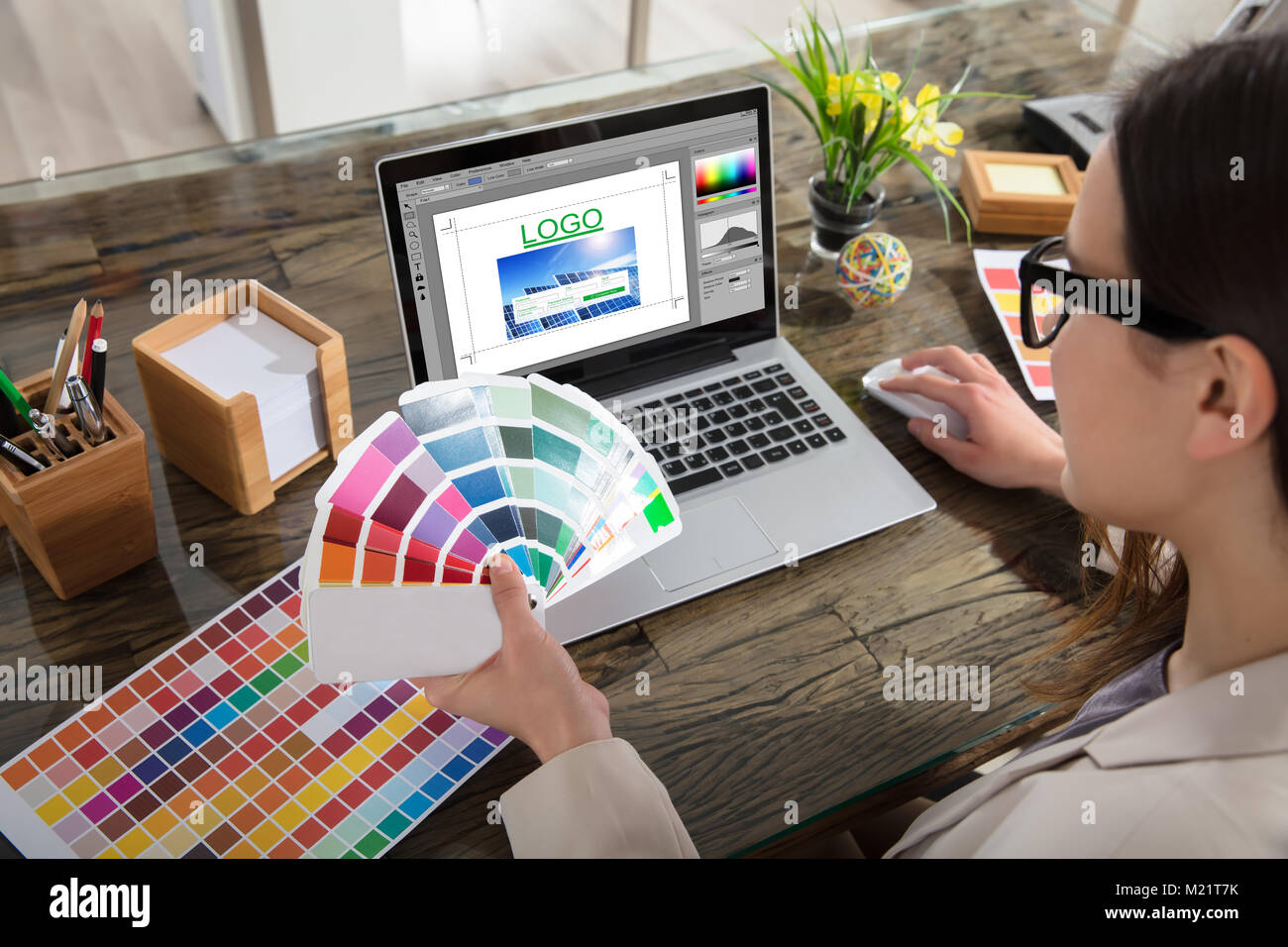Femme tenant un échantillons de couleur à l'aide d'un ordinateur portable avec logiciel de conception de logo sur l'écran Banque D'Images