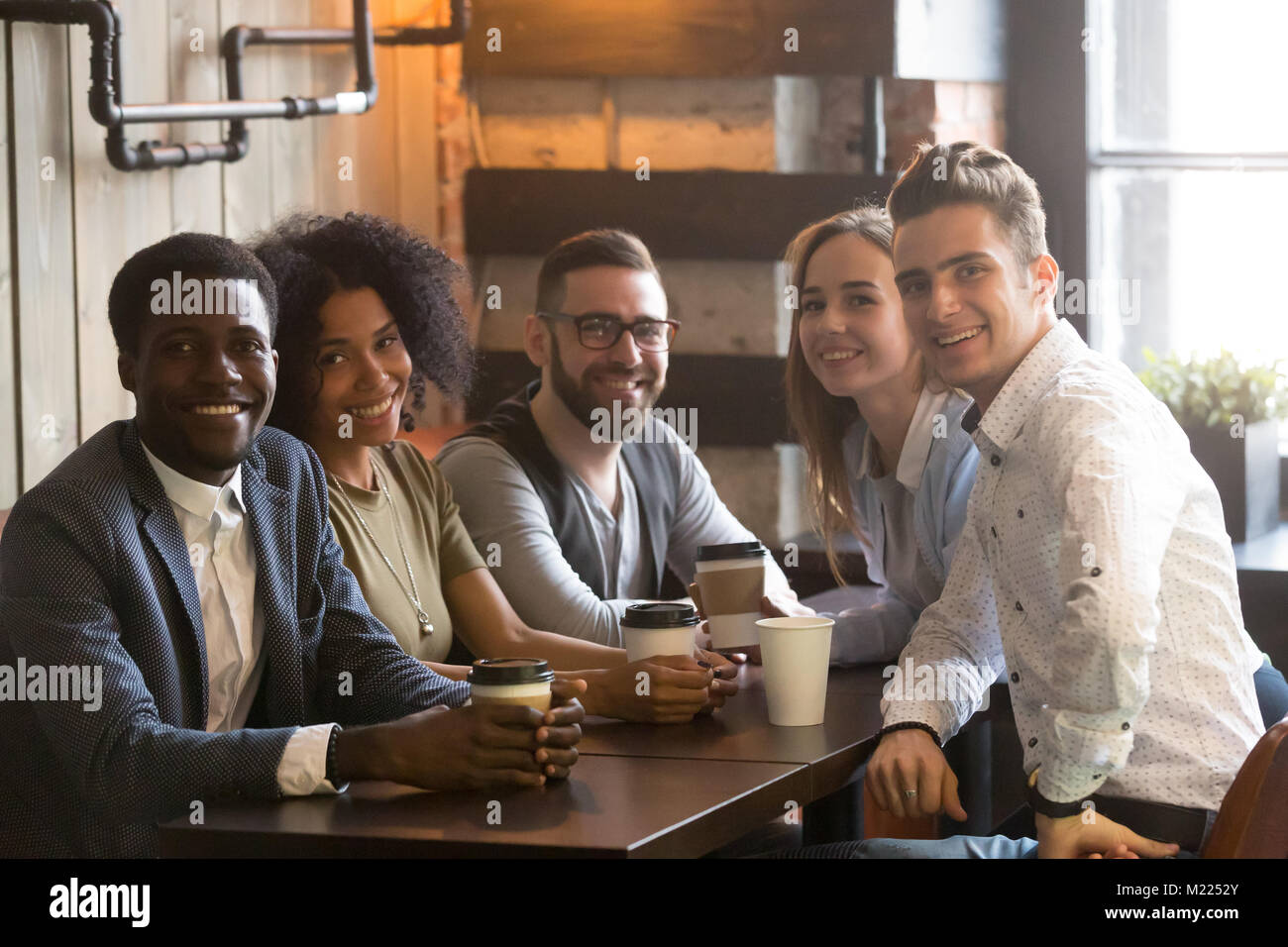 Groupe d'amis multiraciale looking at camera sitting in cafe, por Banque D'Images