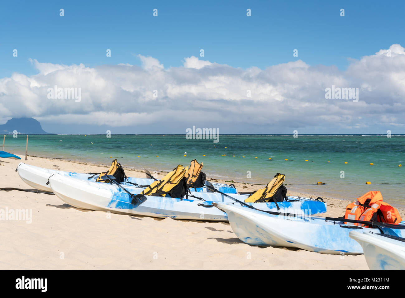 Kayaks bleus et blancs avec des gilets de sauvetage sur plage de sable à l'île Maurice,journée ensoleillée avec des nuages dans le ciel et la montagne l'arrière-plan. Banque D'Images