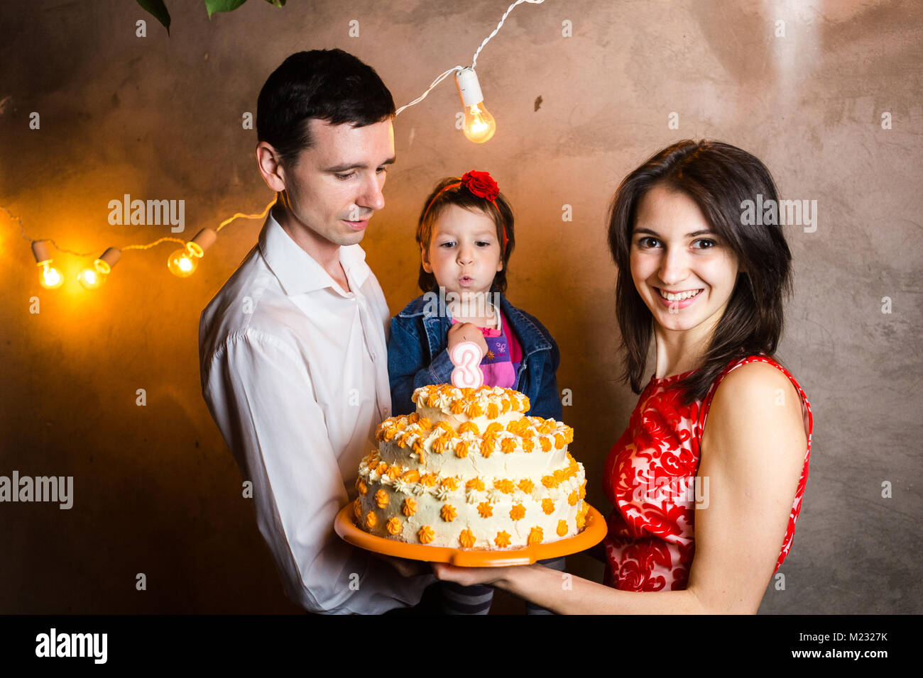 Maison De Famille Theme D Anniversaire Pour Enfants Et Blowing Out Candles On Grand Gateau Jeune Famille De Trois Personnes Debout Et Tenant Ma Fille De 5 Ans Je Photo Stock Alamy
