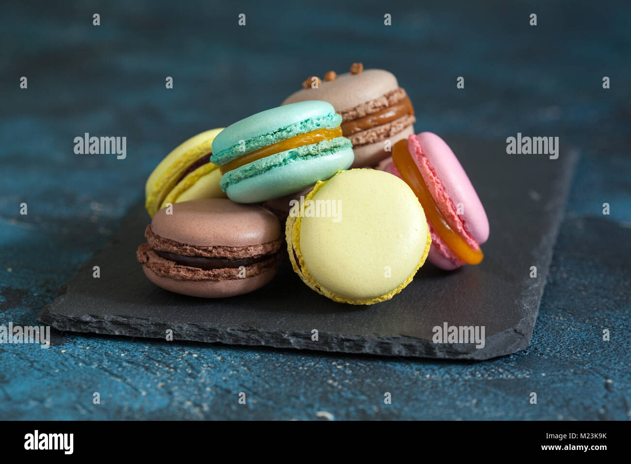 Macaron macaron ou sur fond bleu, biscuits colorés avec différents poids (chocolat, caramel, mangue, cassis). Selective focus Banque D'Images
