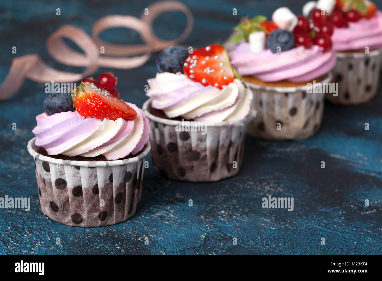 Vanille et chocolat Maison cupcakes avec de la crème et les baies roses cap sur un fond bleu foncé. Banque D'Images