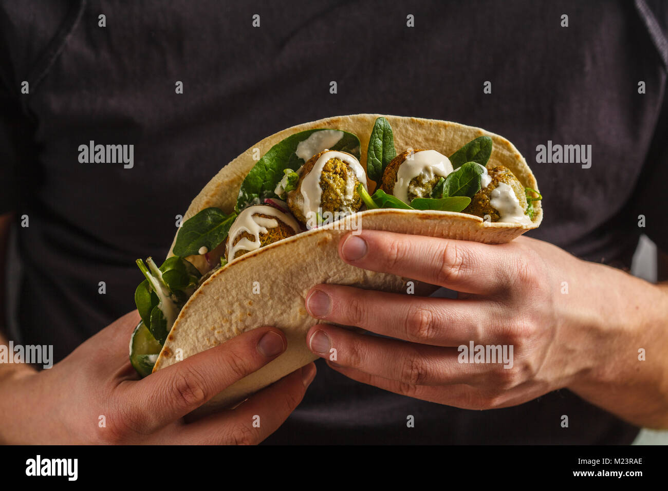 Falafels végétaliens avec légumes et sauce tahini dans la tortilla dans les mains d'un homme. Vegan aliments sains Banque D'Images