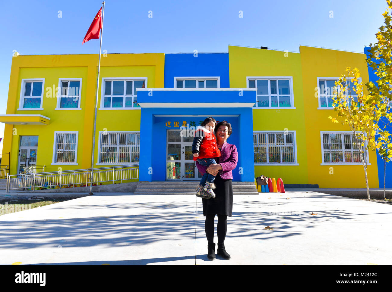 (180204) -- BEIJING, 4 février 2018 (Xinhua) -- Li Yuanmin et un enfant posent pour les photos avant la nouvelle école maternelle publique bâtiment dans Gaimai Village de Yining County, nord-ouest de la Chine, la Région autonome du Xinjiang Uygur, Novembre 22, 2017. Le jardin de 800 mètres carrés peut accueillir plus de 300 enfants du village, il offre gratuitement au long de l'éducation avec des aliments et boissons. Yuanmin Li, un délégué à la 19e Congrès national du Parti communiste chinois (PCC), a servi comme secrétaire du parti du village. Elle a mis beaucoup d'efforts dans la propagation, la route, l'orientation du parti et pol Banque D'Images
