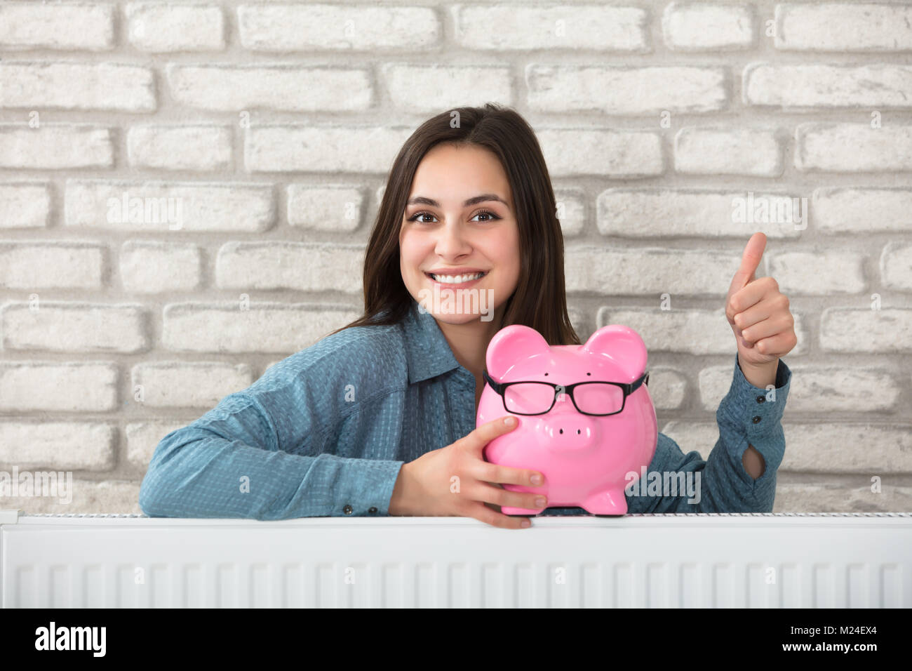 Portrait d'une femme derrière le radiateur de chauffage Holding Piggy Bank Banque D'Images