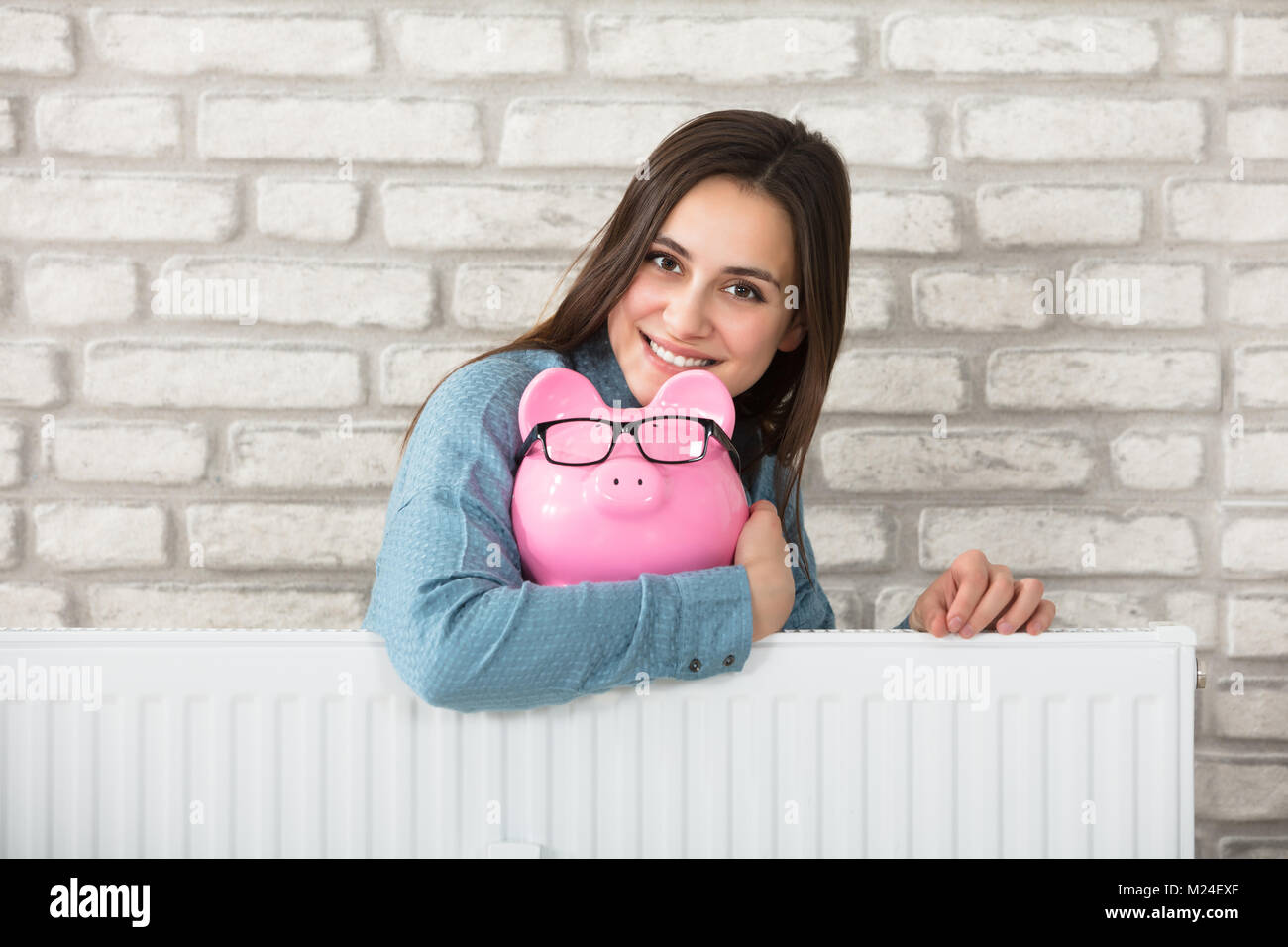 Portrait d'une femme derrière le radiateur de chauffage Holding Piggy Bank Banque D'Images